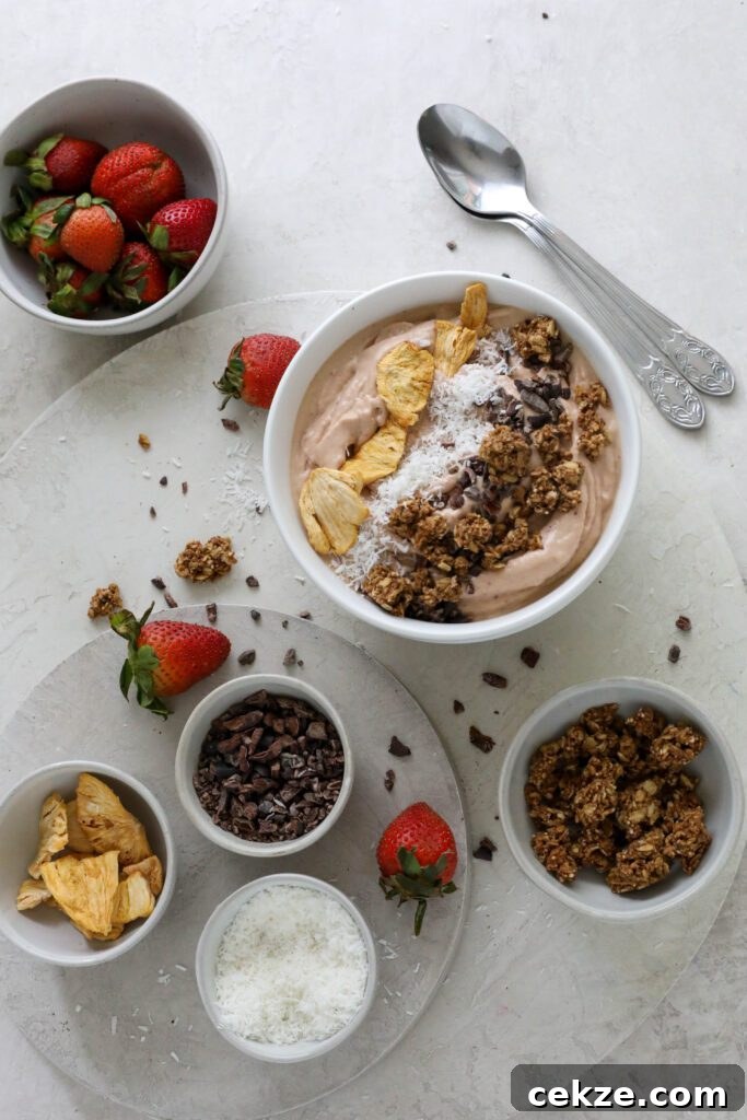 Strawberry Mango Smoothie Bowl Recipe for Creamy Tropical Breakfast 7 Strawberry Mango Smoothie Bowl served in bowl topped with dried pineapple, shredded coconut, and granola with fresh strawberries on the side