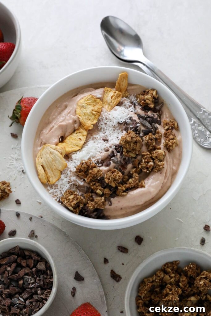 Strawberry Mango Smoothie Bowl Recipe for Creamy Tropical Breakfast 8 Strawberry Mango Smoothie Bowl served in bowl topped with dried pineapple, shredded coconut, and granola with fresh strawberries on the side