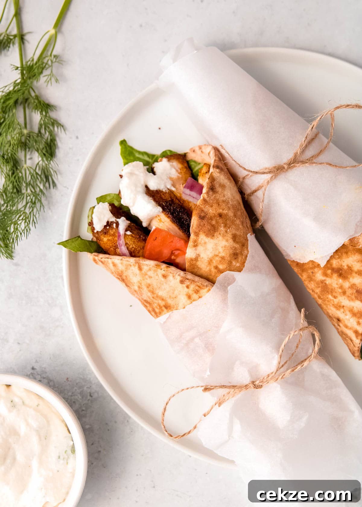 overhead shot showing two chicken shawarma pita wraps with veggies on a white plate with a side of creamy yogurt sauce