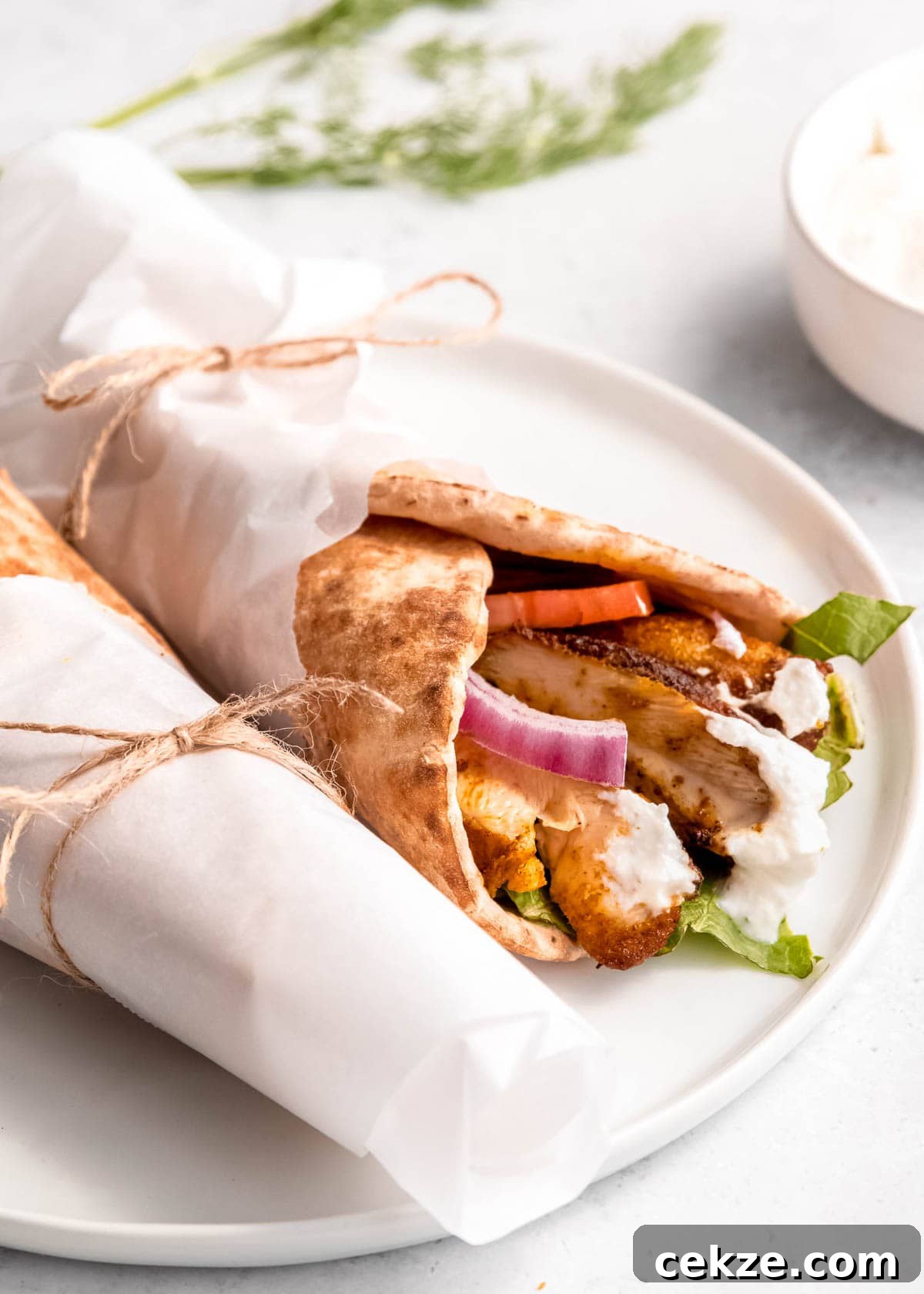 two chicken shawarma pita wraps wrapped in parchment paper on a white plate