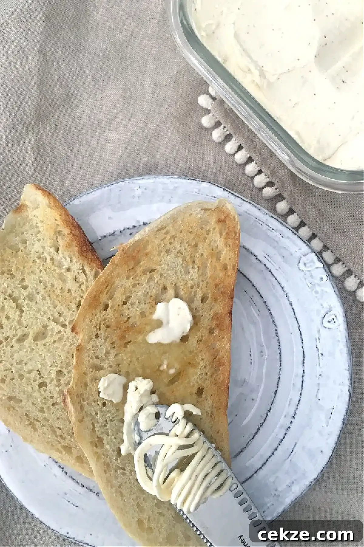 dairy free butter spread on toast, on a rustic white plate next to a square glass container of dairy free butter.