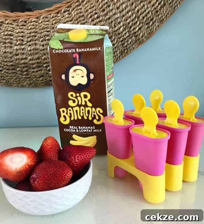 A bowl of strawberries and a container of chocolate milk beside freezer pop molds.