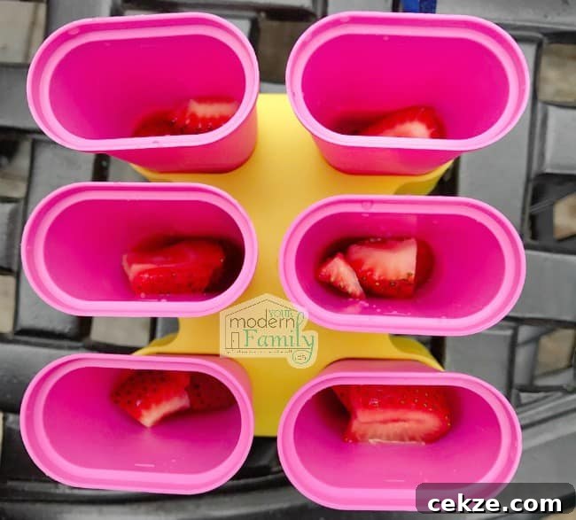 Top view of open freezer pop molds with strawberries in them.