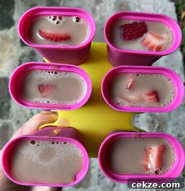 A close up of a freezer pop molds filled with strawberries and banana chocolate milk.