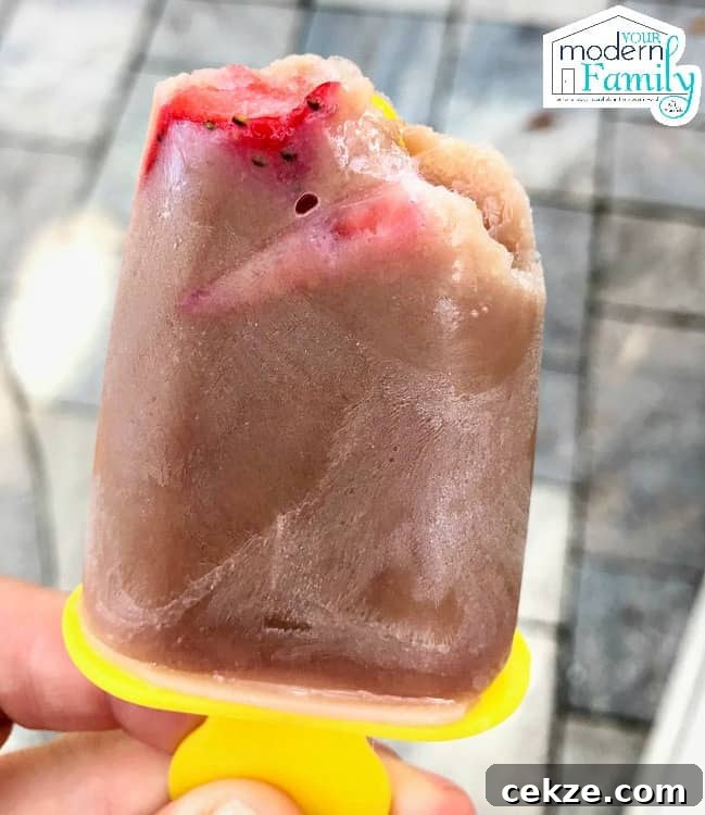 A close up of a person holding a frozen chocolate covered strawberry banana freezer pop.