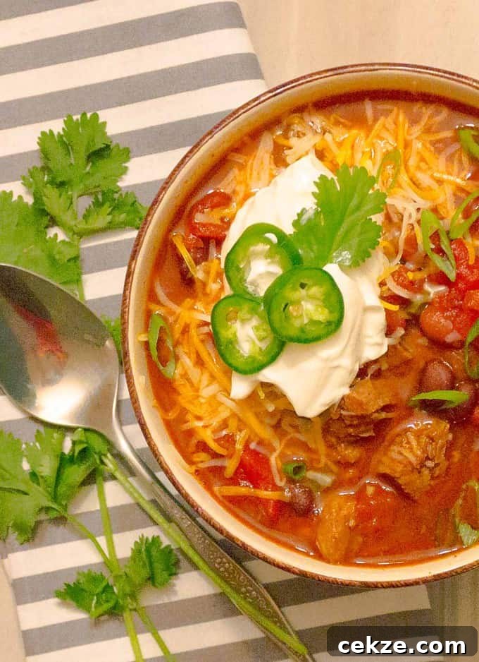 Instant Pot Red Pork Carnitas Chili Recipe 3 Instant Pot Pressure Cooker Red Pork Chili in a bowl with ganishings on white wood planks and a gray striped napkin.