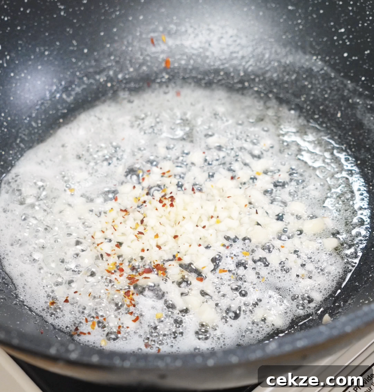 Minced garlic sizzling in melted butter with red chili flakes, releasing a fragrant aroma.