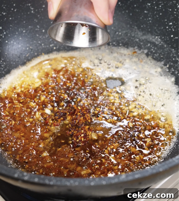 Soy sauce and chili oil being added to the pan, blending with the garlic butter to create a spicy, umami-rich base.