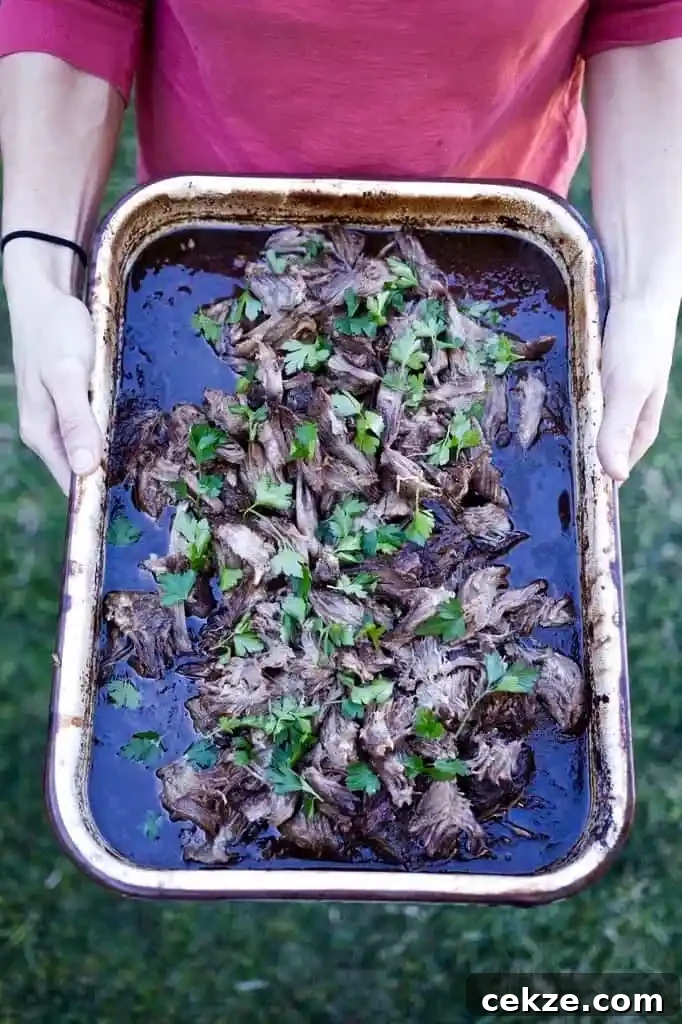 A woman in a pink shirt holding a white tray of shredded beef barbacoa that is topped with parsley leaves. 