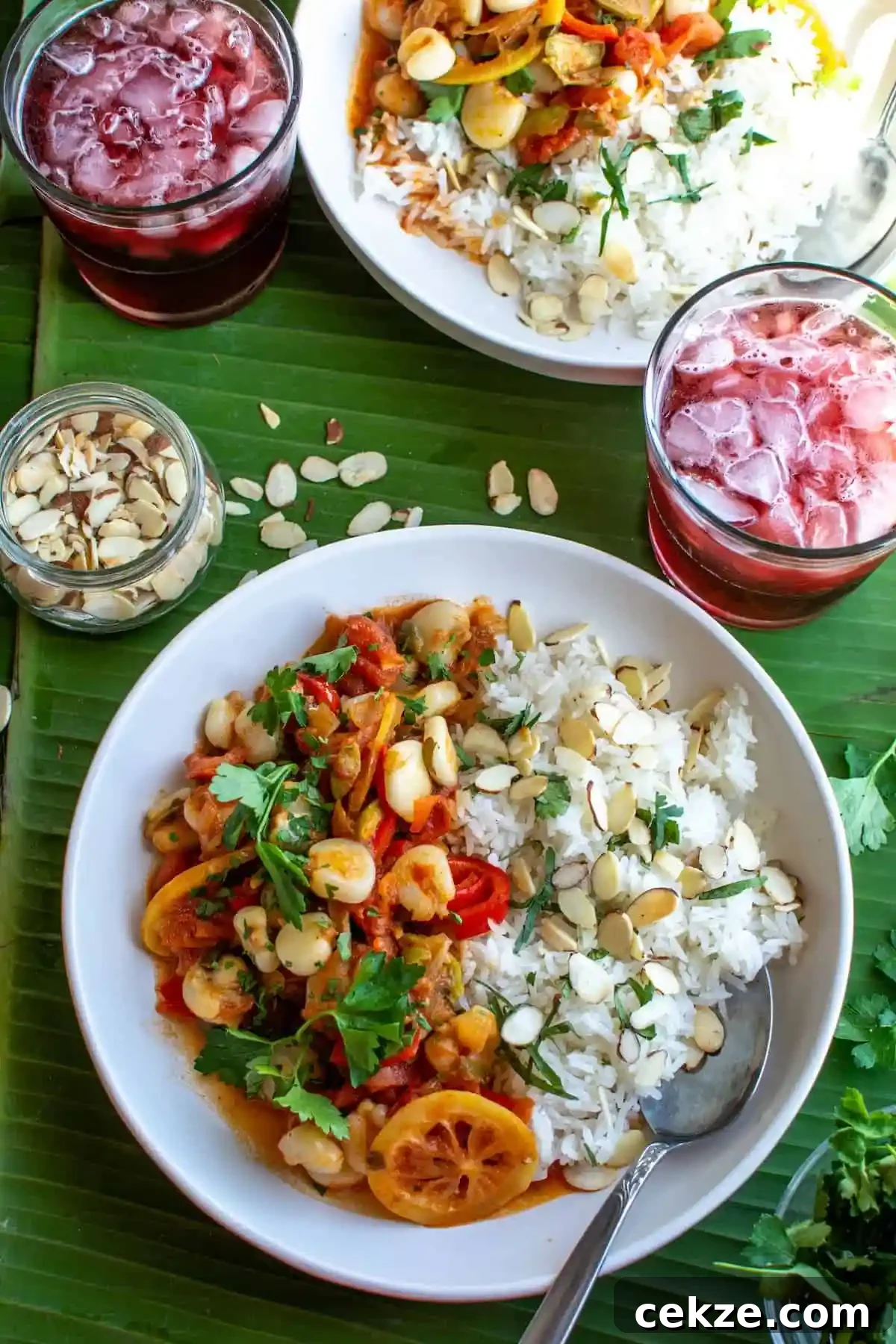Two plates of hominy and rice sprinkled with sliced almonds sitting on a green banana leaf with two glasses. 