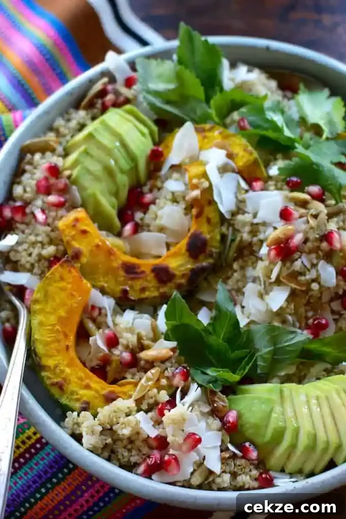 A ceramic bowl filled with quinoa topped with sliced avocado, roasted kabocha squash, shredded coconut, and pomegranate. 