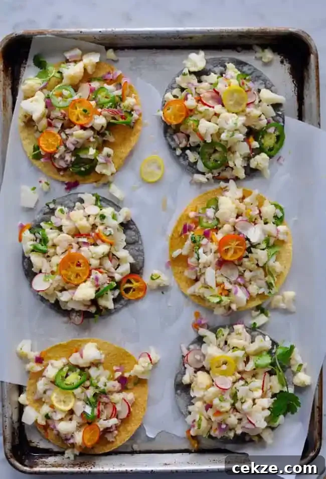 A baking sheet with a piece of white parchment paper on it that is topped with 6 tostadas that have cauliflower ceviche. 