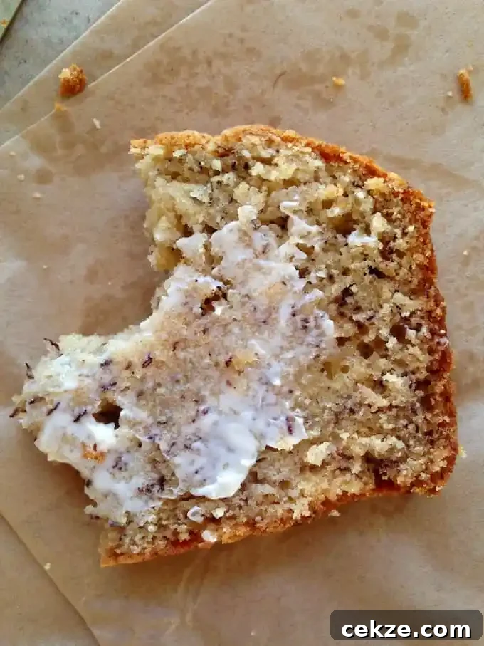A piece of banana bread with a bite taken out of one side and smeared with butter. It is sitting on a piece of brown parchment. 