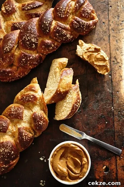 3 loaves of pretzel challah on a wood table with one of them sliced and a ramekin of adobo butter and a butter knife. 
