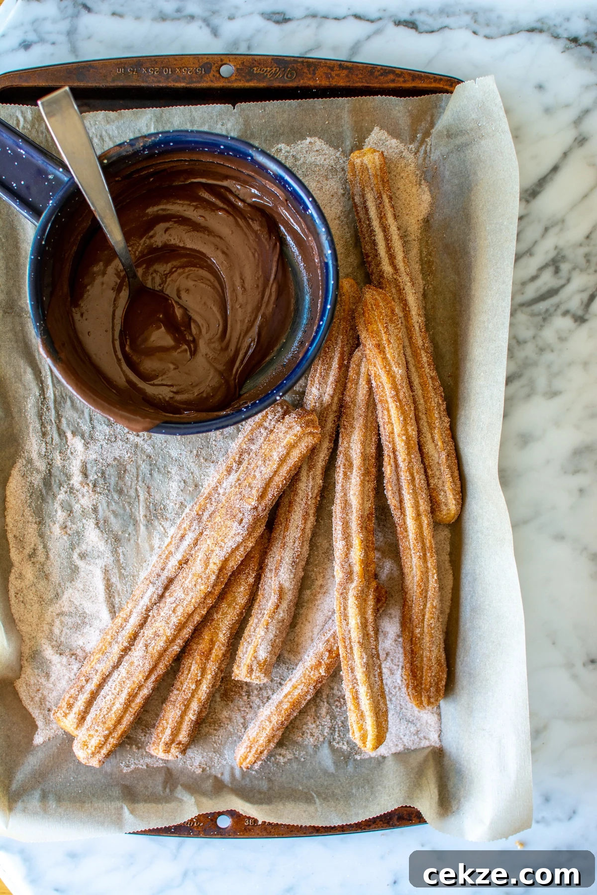 A baking sheet covered with a piece of parchment paper and several long churros on it dusted with cinnamon sugar. 