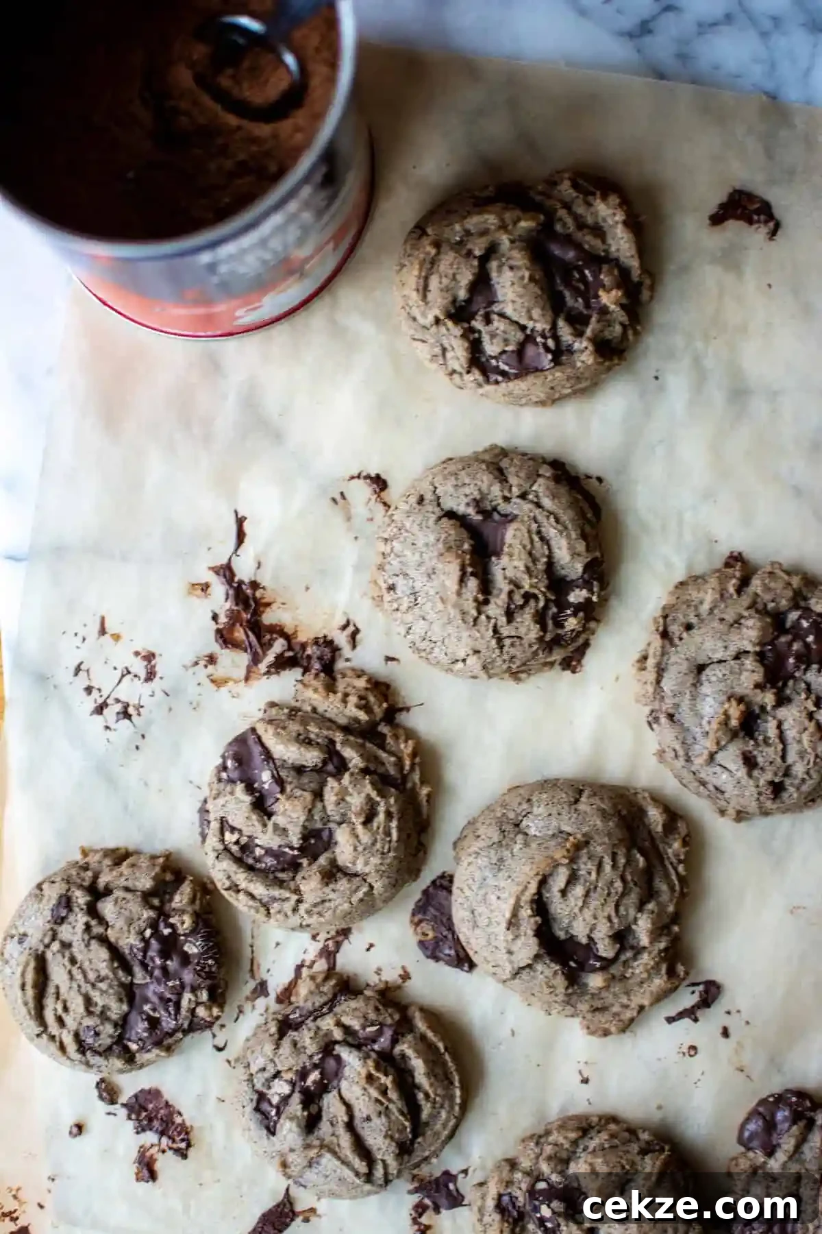 Several chocolate chip cookies on a piece of parchment paper with a blue and red can of coffee next to them. 