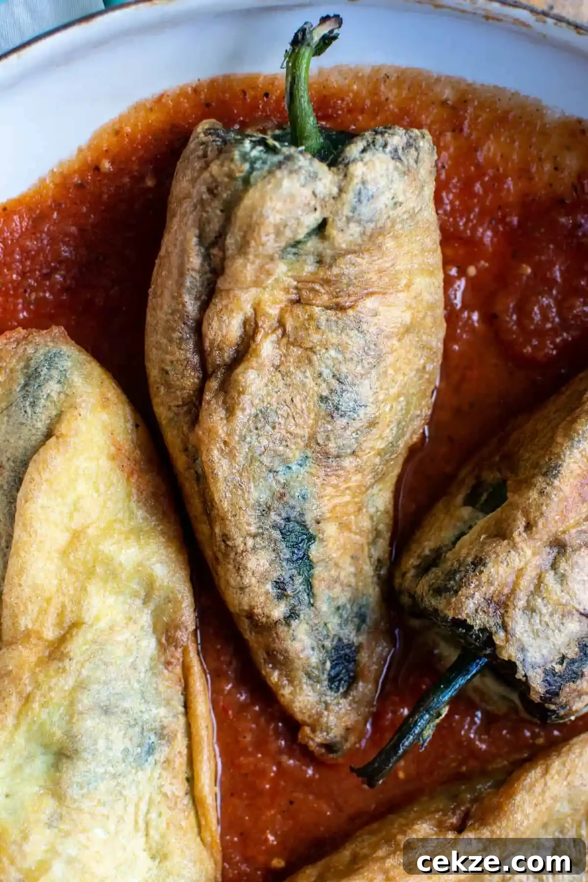 3 Chiles Rellenos sitting in a pool of tomato sauce on a white platter. 