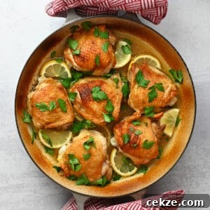 An overhead shot of two hands holding a skillet filled with lemon garlic chicken thighs with two red and white kitchen towels.