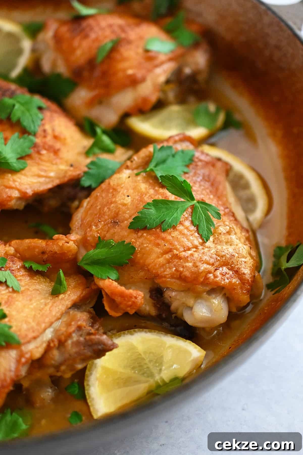 A closeup view of lemon garlic chicken thighs in a skillet with golden brown skin.