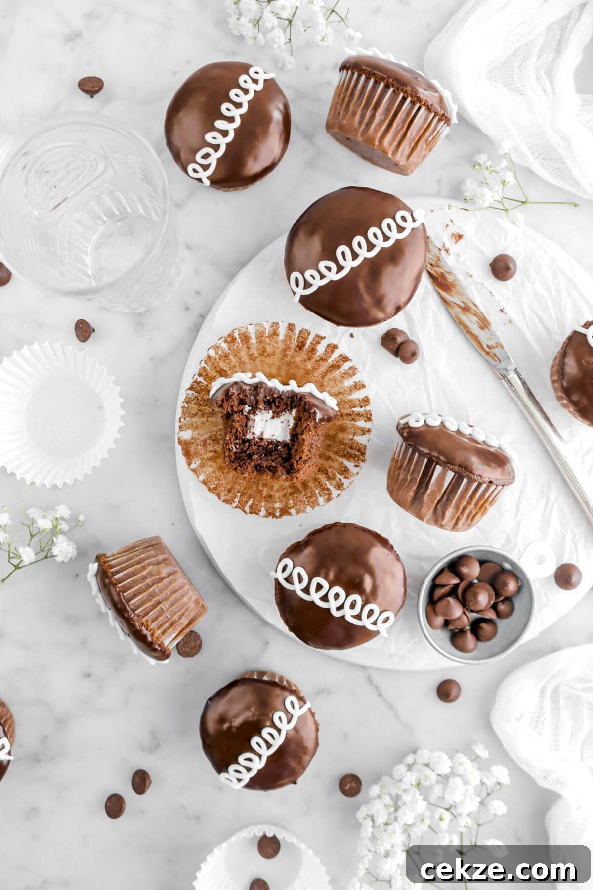 overhead shot of nine cupcakes with bite missing from one cupcake on white plate with chocolate chips and flowers around.