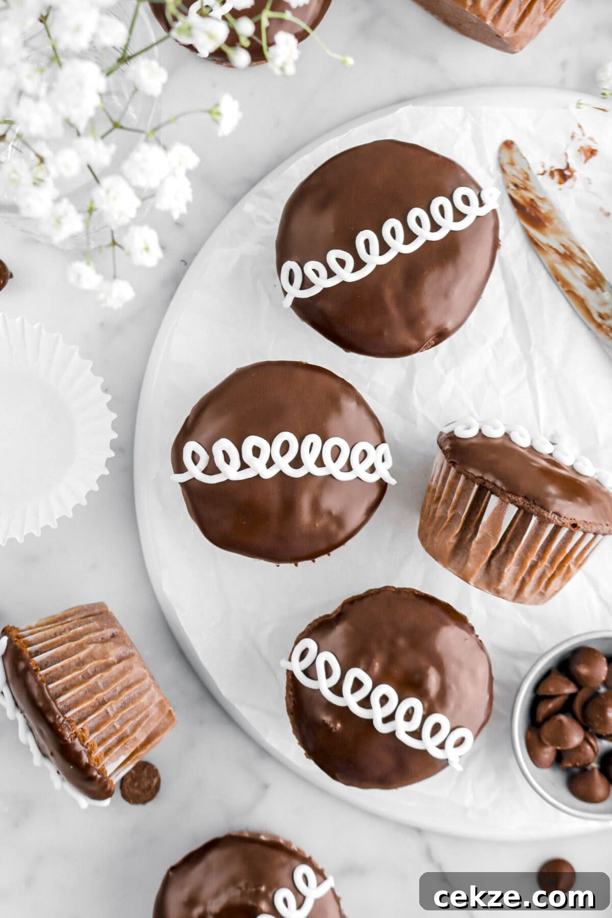 close up of four chocolate cupcakes on upside down plate with more cupcakes around on marble surface with white flowers.