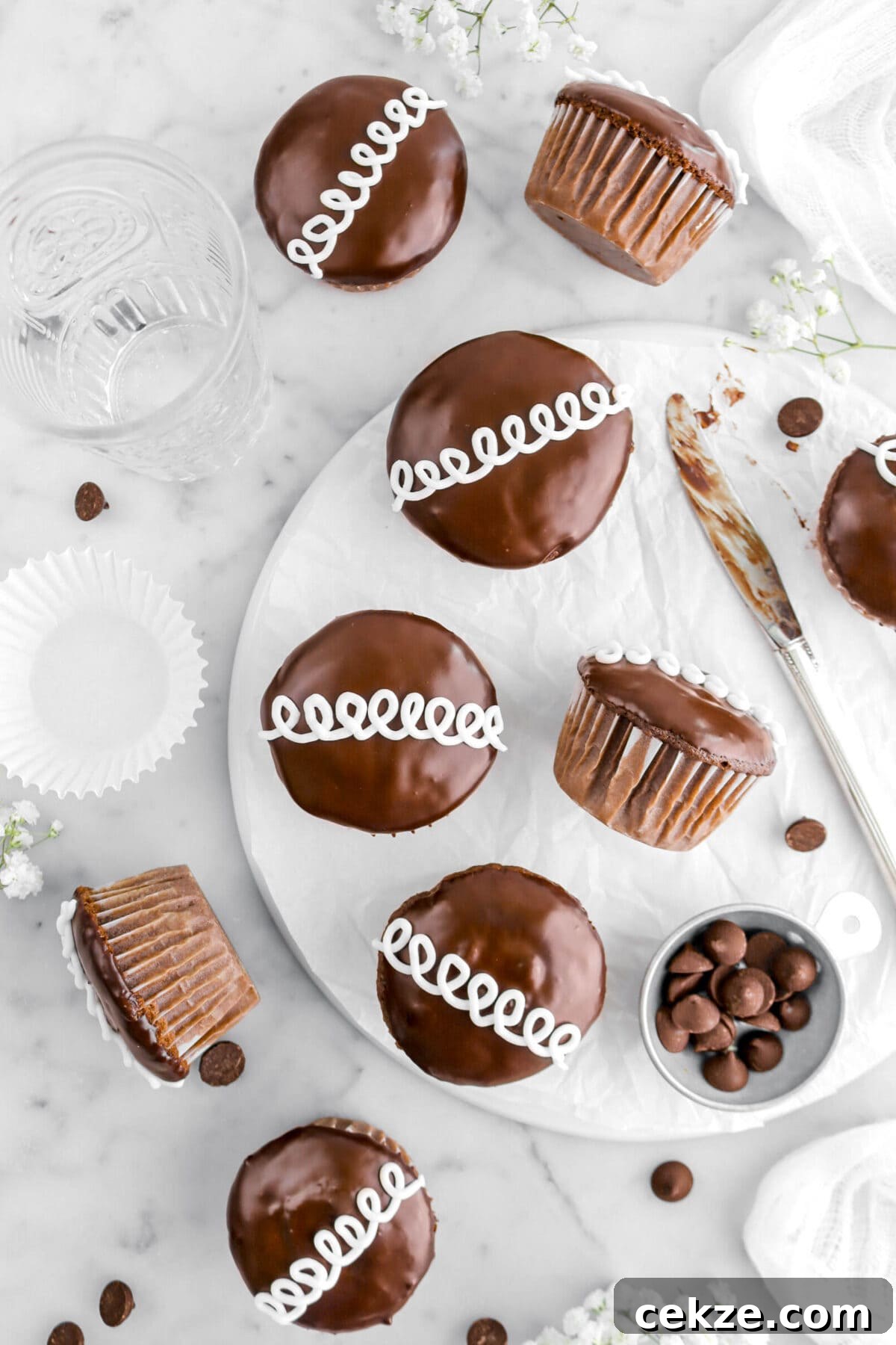 five chocolate cupcakes on upside down plate with one turned on it's side, a knife and measuring cup of chocolate chips beside, with four more cupcakes around on marble surface.