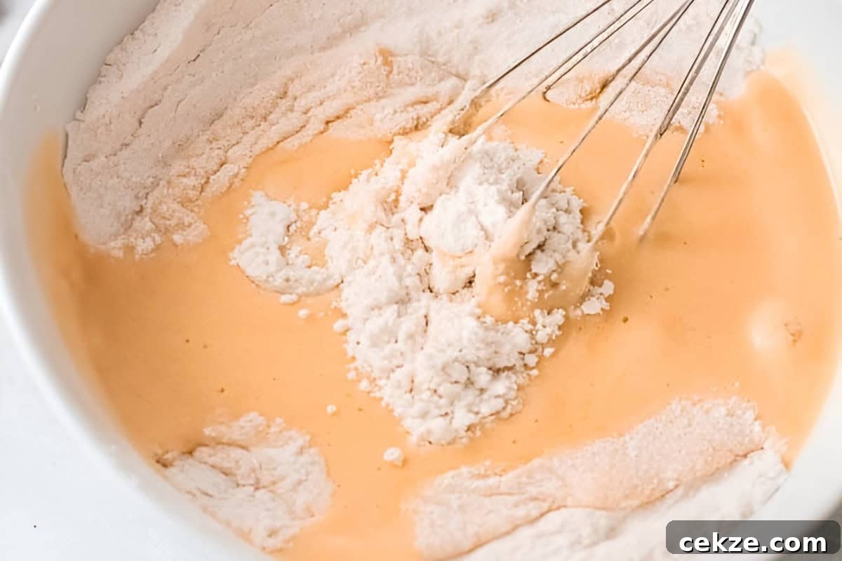 whisking wet and dry ingredients for olive oil cake in a white bowl.