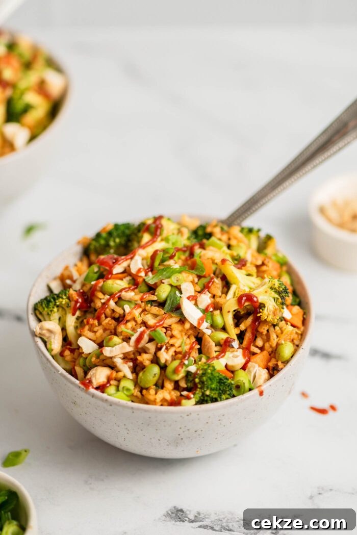 Bowl of fried rice with broccoli, carrot, edamame and green onion topped with chopped cashews.