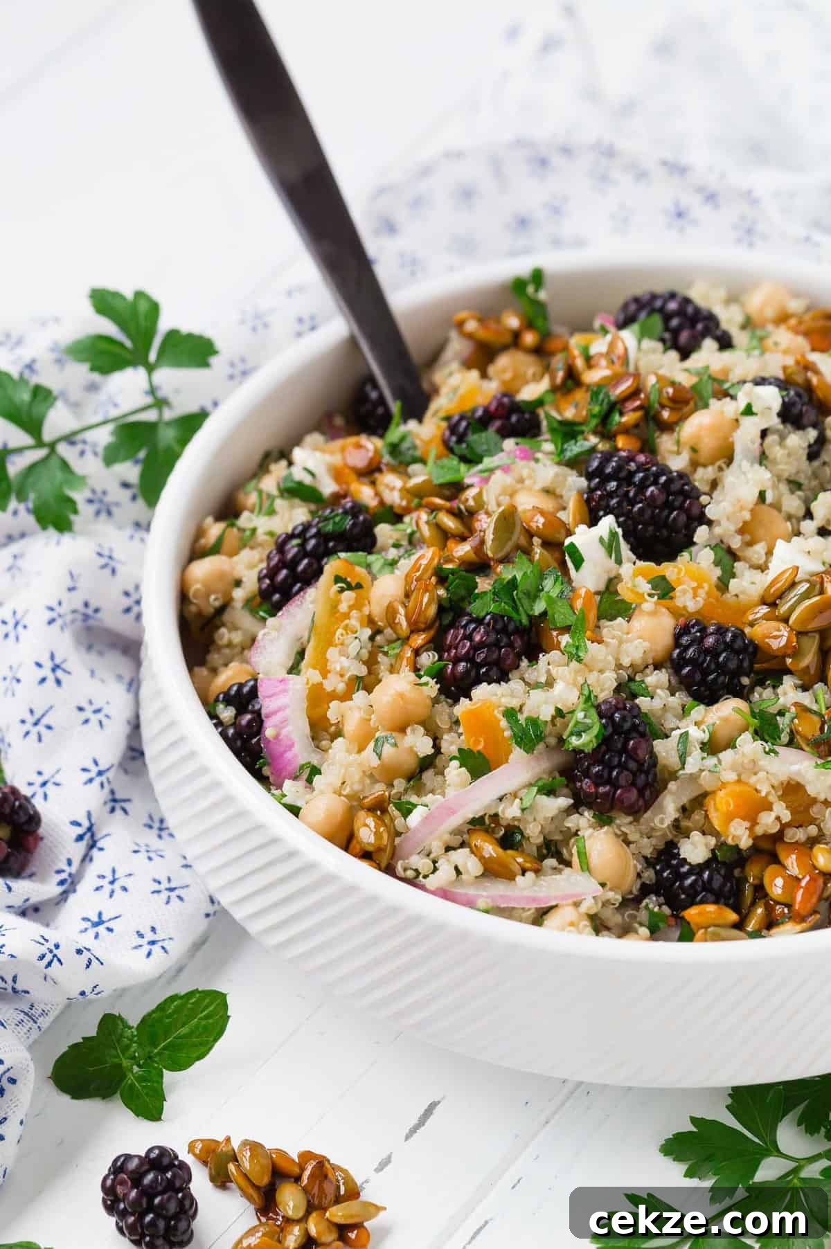 Quinoa and Chickpea Salad with Blackberries and Candied Pepitas 7 Hearty quinoa salad in a white bowl with a black spoon.