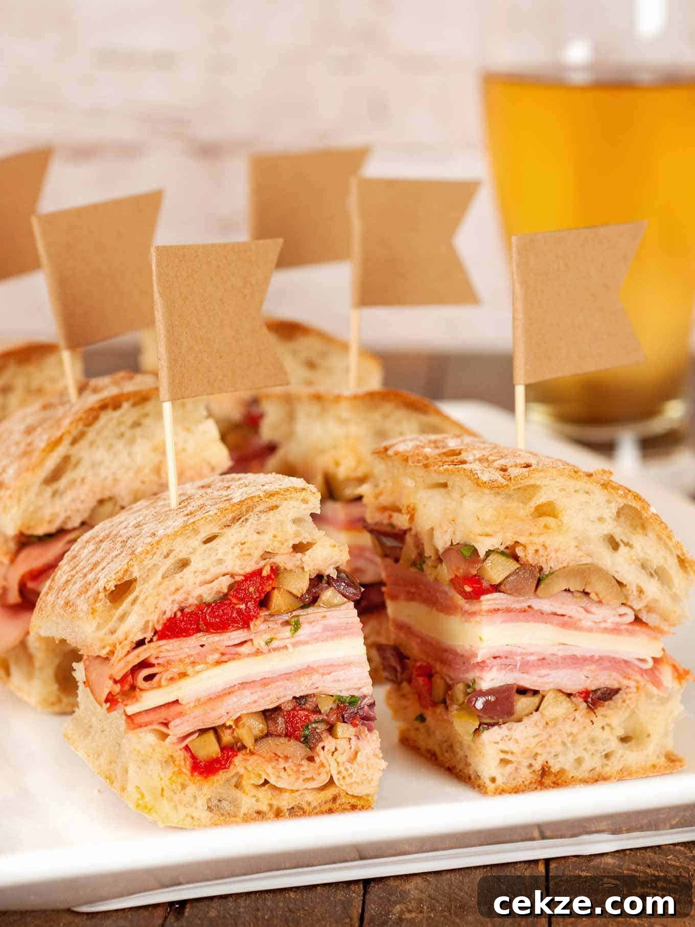 Party-sized portions of muffaletta sandwiches stacked with layers of deli meats, cheese, and olive salad on crusty bread, each topped with a small flag toothpick.