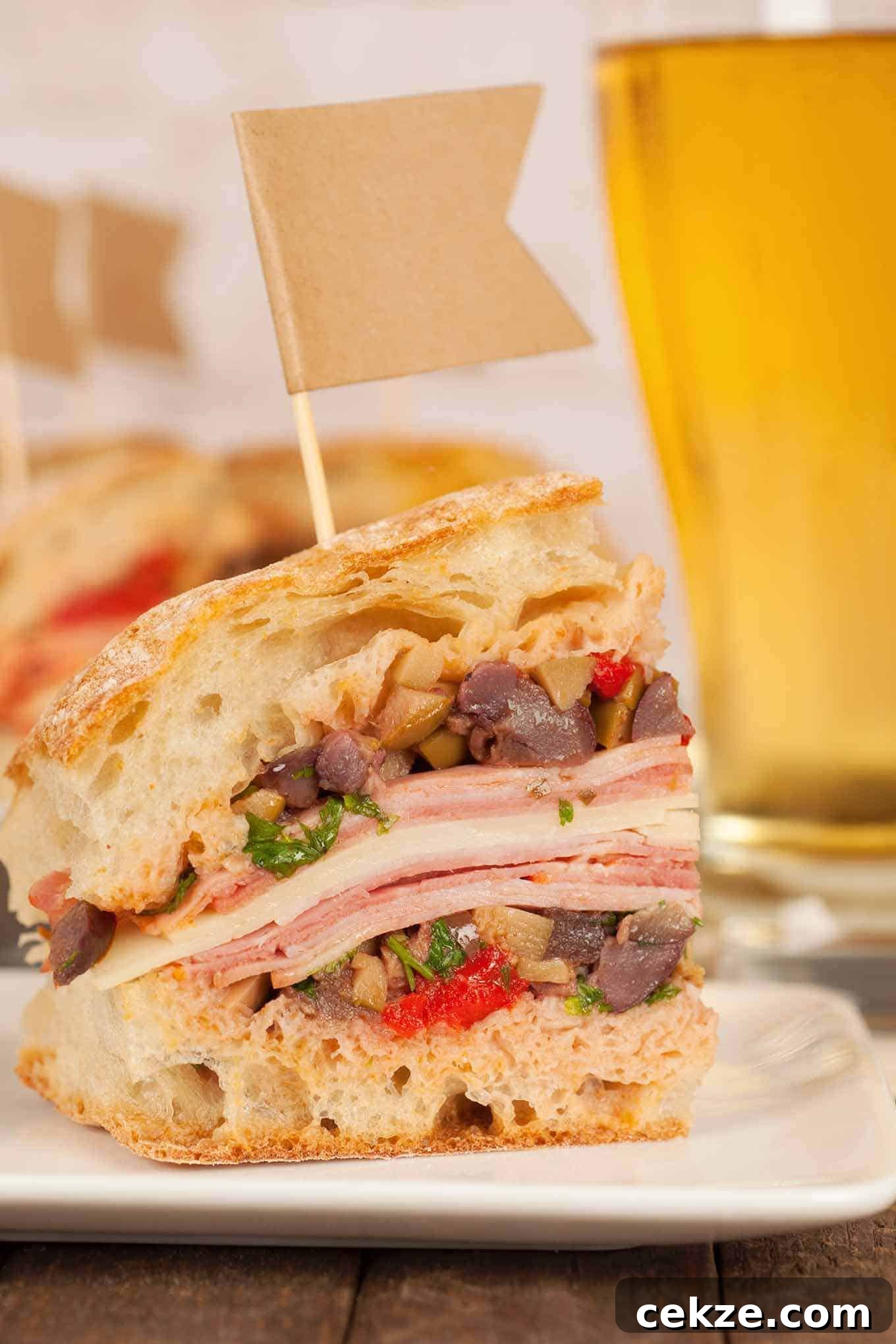 A close view of a cut muffaletta sandwich stacked with layers of deli meats, cheese, and olive salad on crusty bread.