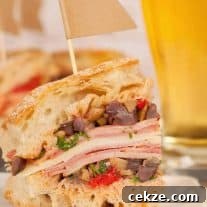 A close view of a cut muffaletta sandwich stacked with layers of deli meats, cheese, and olive salad on crusty bread.