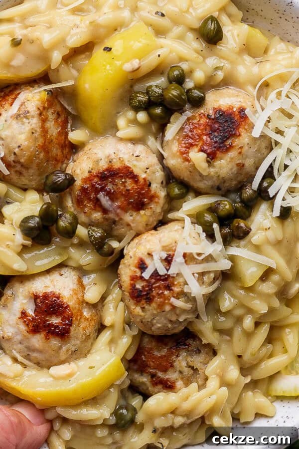 A bowl of chicken piccata meatballs in orzo with capers and parmesan cheese.