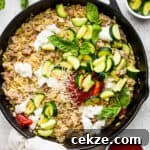 Top down shot of a cast iron skillet filled with a sausage zucchini skillet with cheesy orzo and topped with marinara and fresh basil.