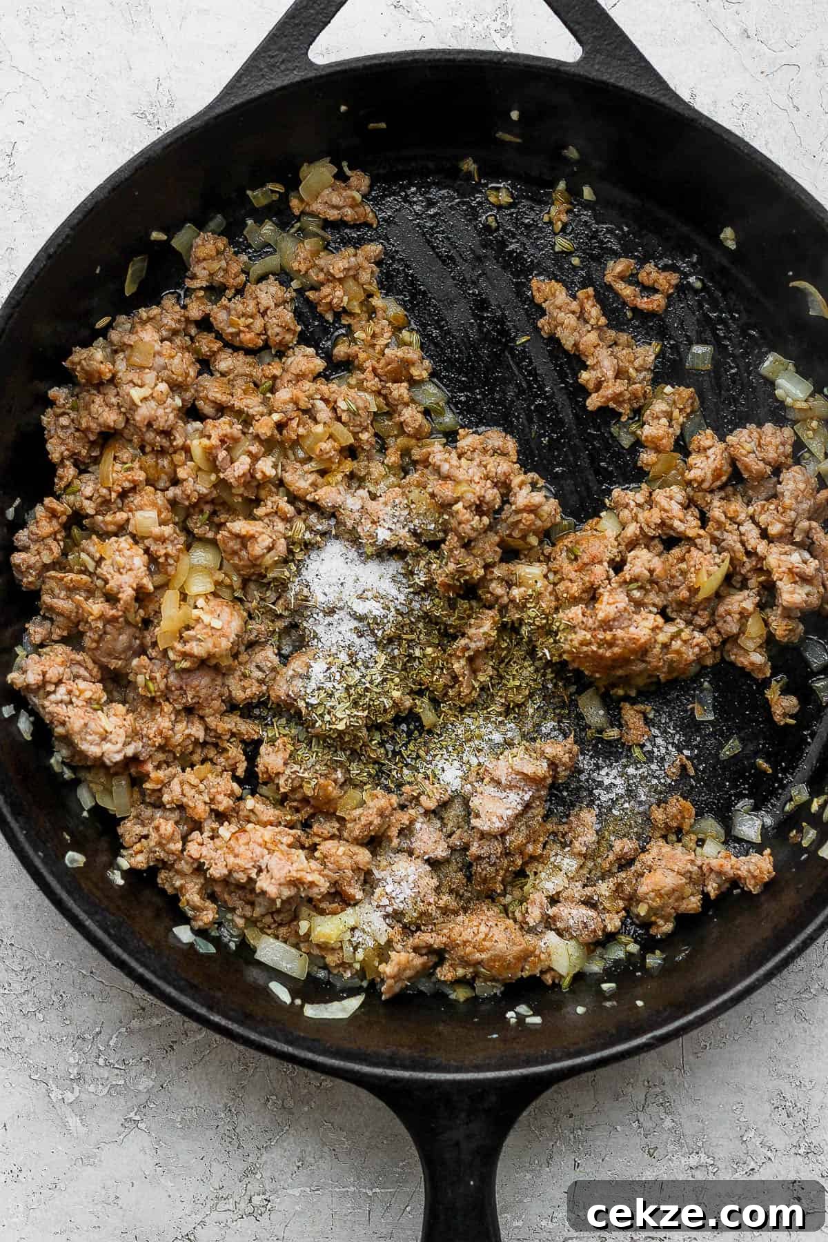 A skillet with browned Italian sausage and seasonings added.