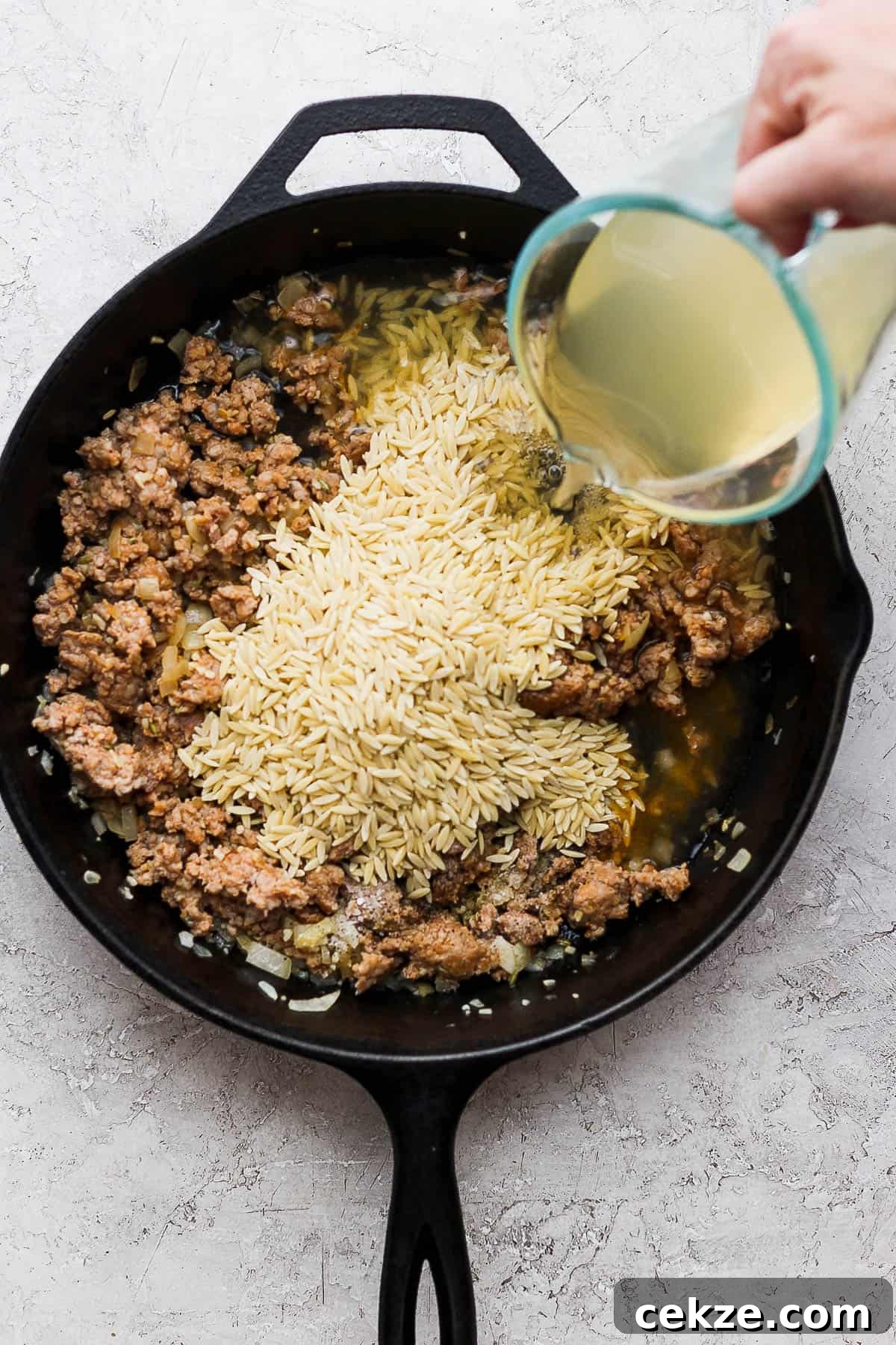 Dry orzo added to the skillet and chicken broth being poured in.
