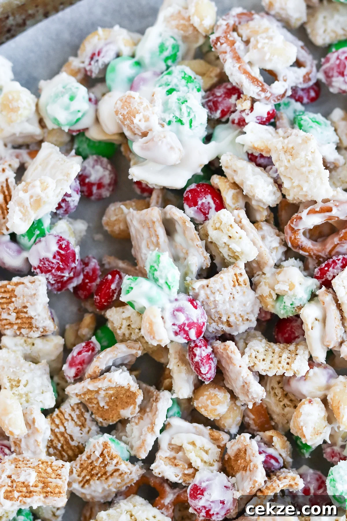 A close-up image of a white trash candy mix, consisting of golden grahams cereal, chex cereal, peanuts, m&m's, pretzels coated in melted white chocolate.