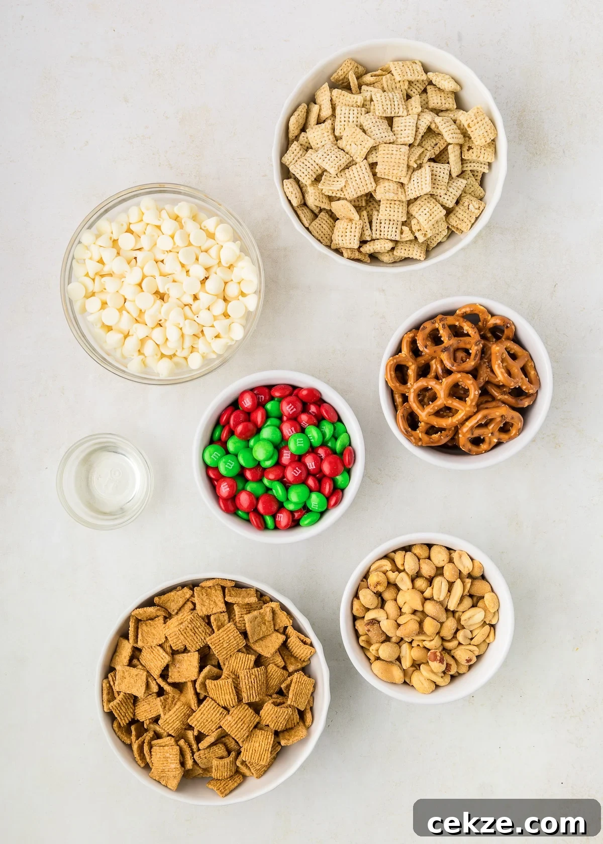ingredient shot for white trash showing a bowl of Chex cereal, pretzels, holiday m&m's, peanuts, Golden Grahams and oil. 