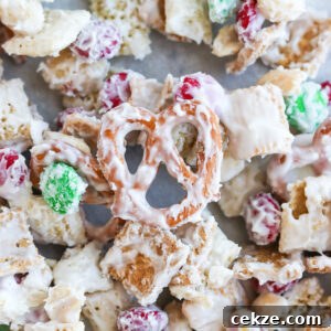 A close-up image of a white trash candy mix, consisting of golden grahams cereal, chex cereal, peanuts, m&m's, pretzels coated in melted white chocolate.