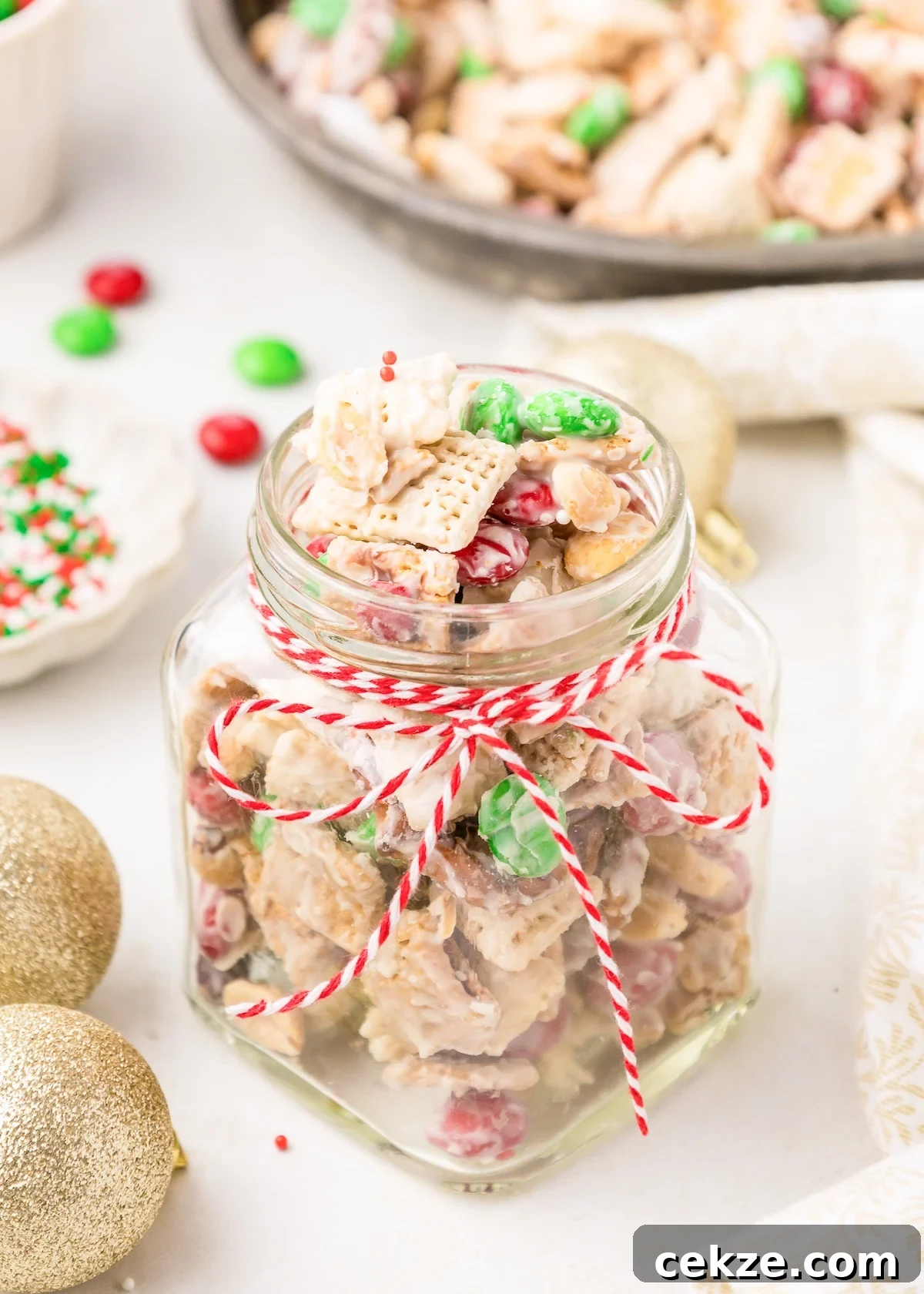 a glass jar full of holiday white trash tied with a decorative christmas ribbon. the background has ornaments and extra christmas sprinkles. 