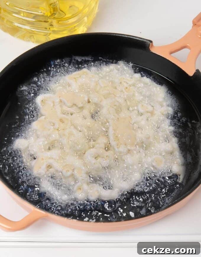 funnel cake batter being fried in hot oil in pink skillet