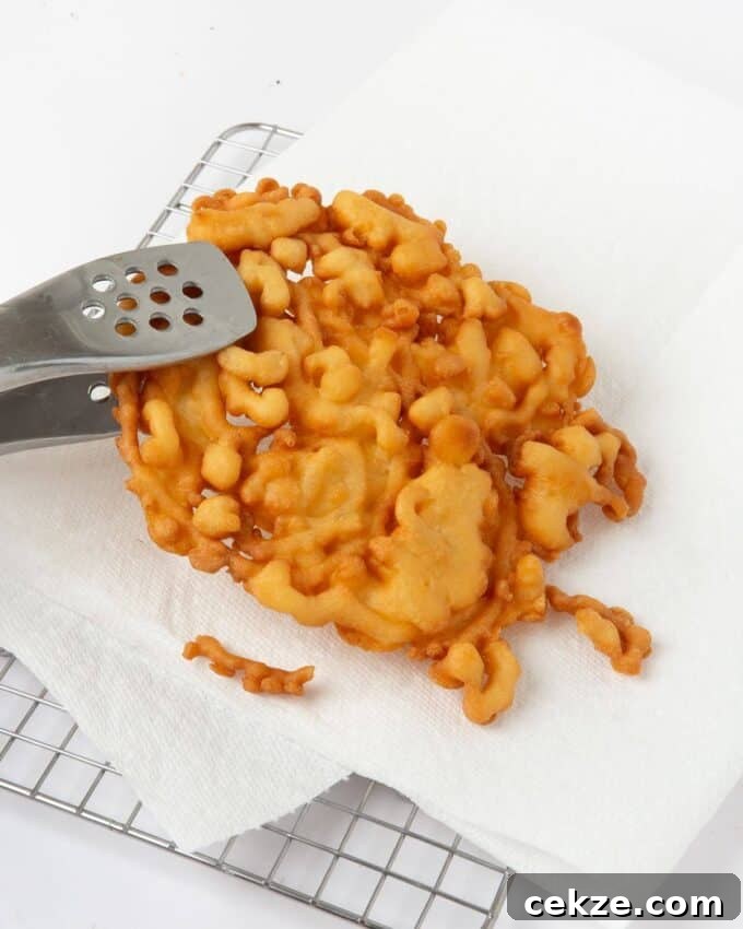 funnel cake being removed from fryer onto paper towel lined plate