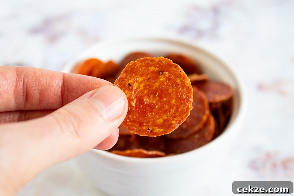 fingers holding up keto pepperoni chips in front of a bowl