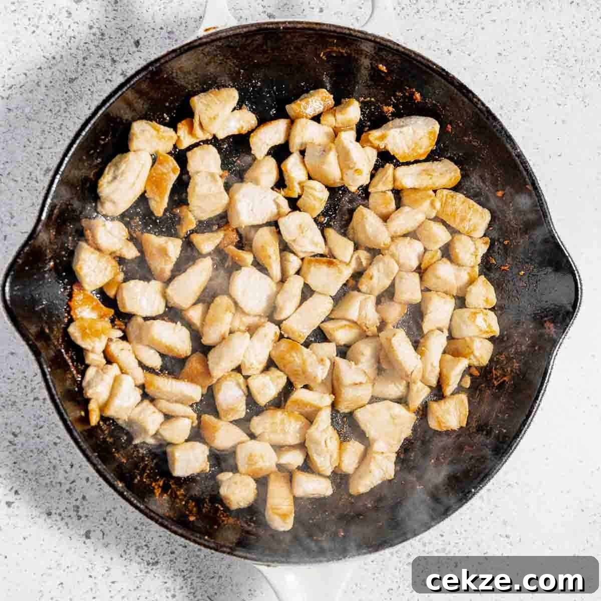 Overhead view of process shot 1 - cooking chicken in a large skillet with olive oil.