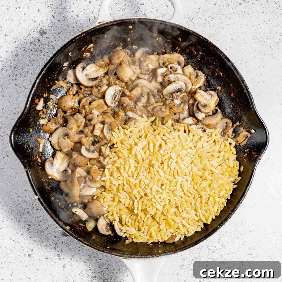 Overhead view of process shot 3 - adding salt, pepper, and orzo to skillet and sautéing for a few more minutes.