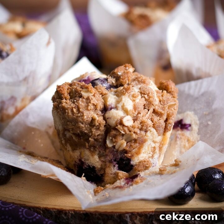 A sour cream streusel blueberry muffin on a wooden tray surrounded by more muffins.