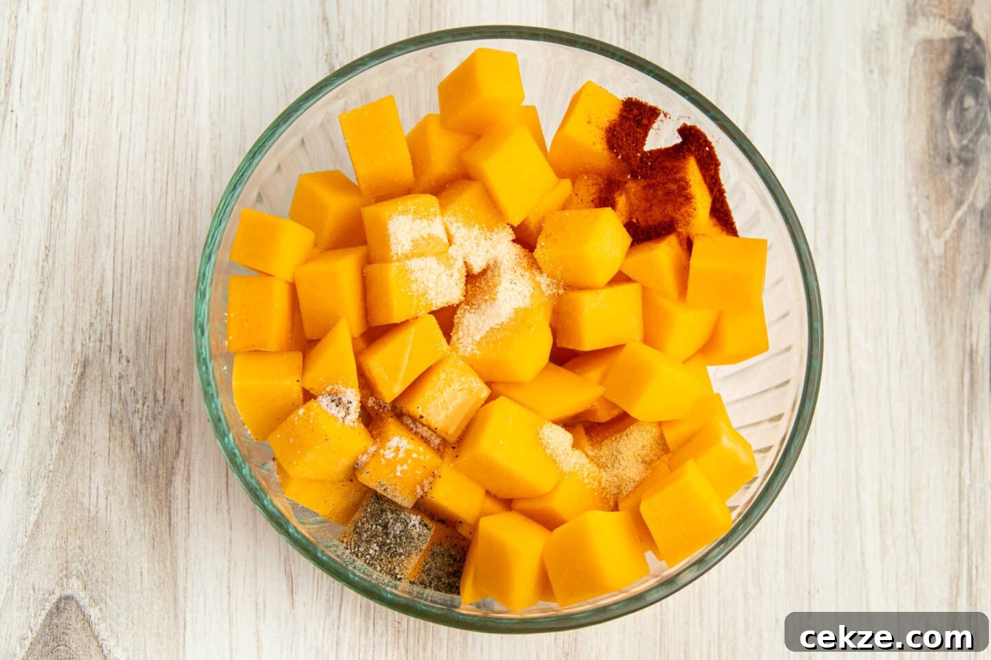 This is a picture of a bowl filled with raw butternut squash and spices on top.