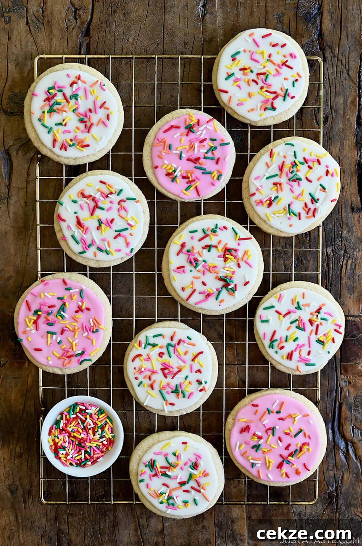 Perfect Sugar Cookie Icing Recipe for Smooth, Glossy Frosting 2 Sugar cookies with white and pink icing and rainbow sprinkles atop a wire rack.