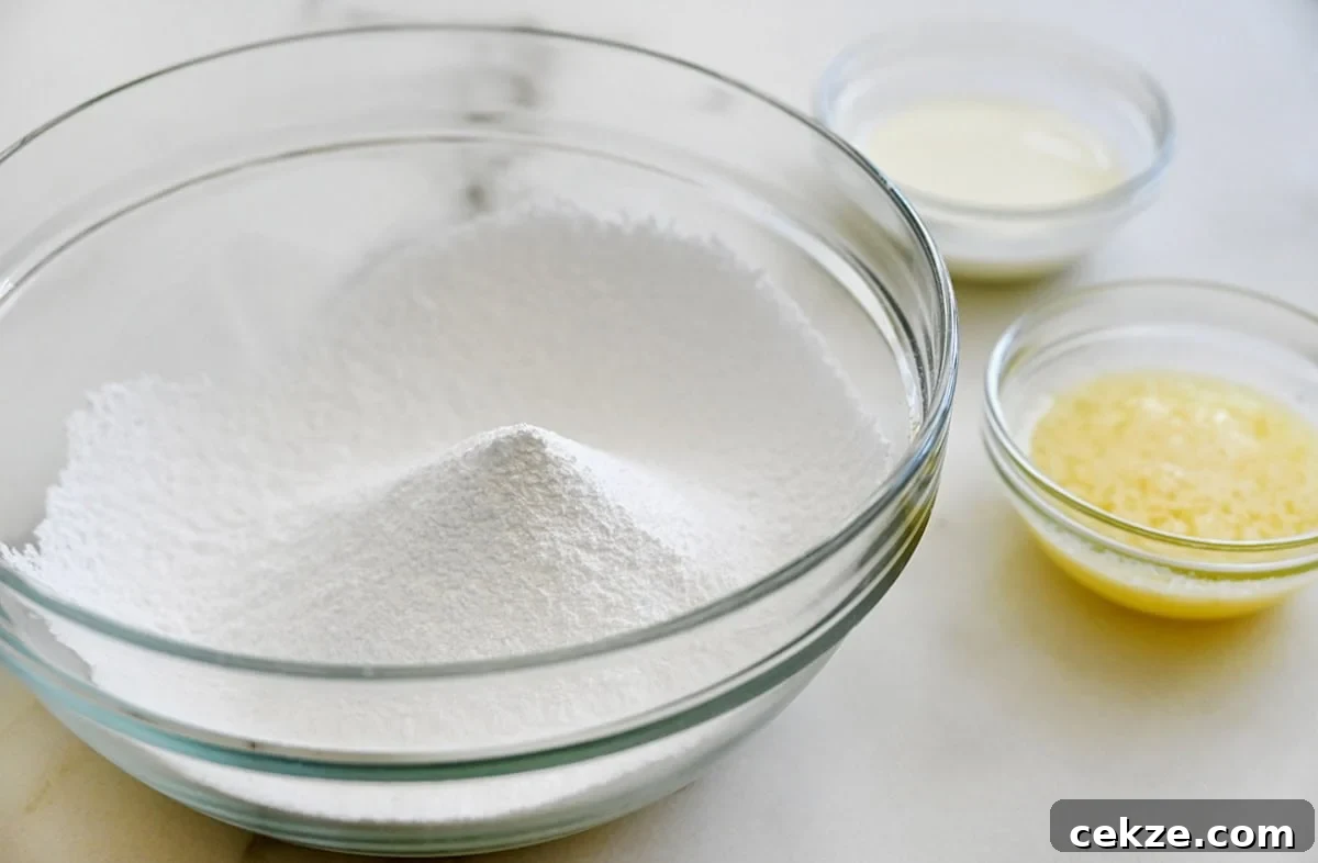 Perfect Sugar Cookie Icing Recipe for Smooth, Glossy Frosting 4 A clear bowl containing confectioners’ sugar next to two small bowls containing melted butter and whole milk.
