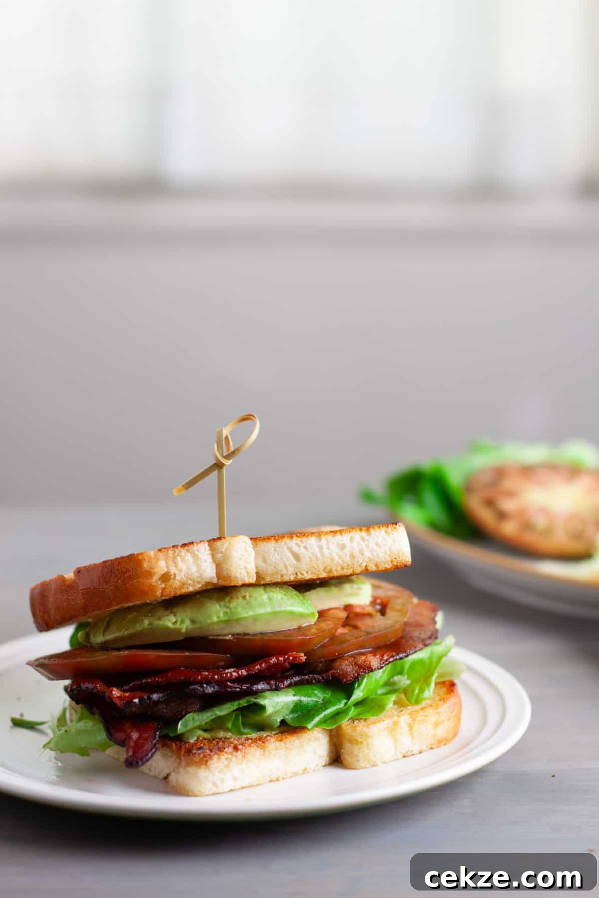 An avocado BLT on a toasted white bread on top of a white plate.